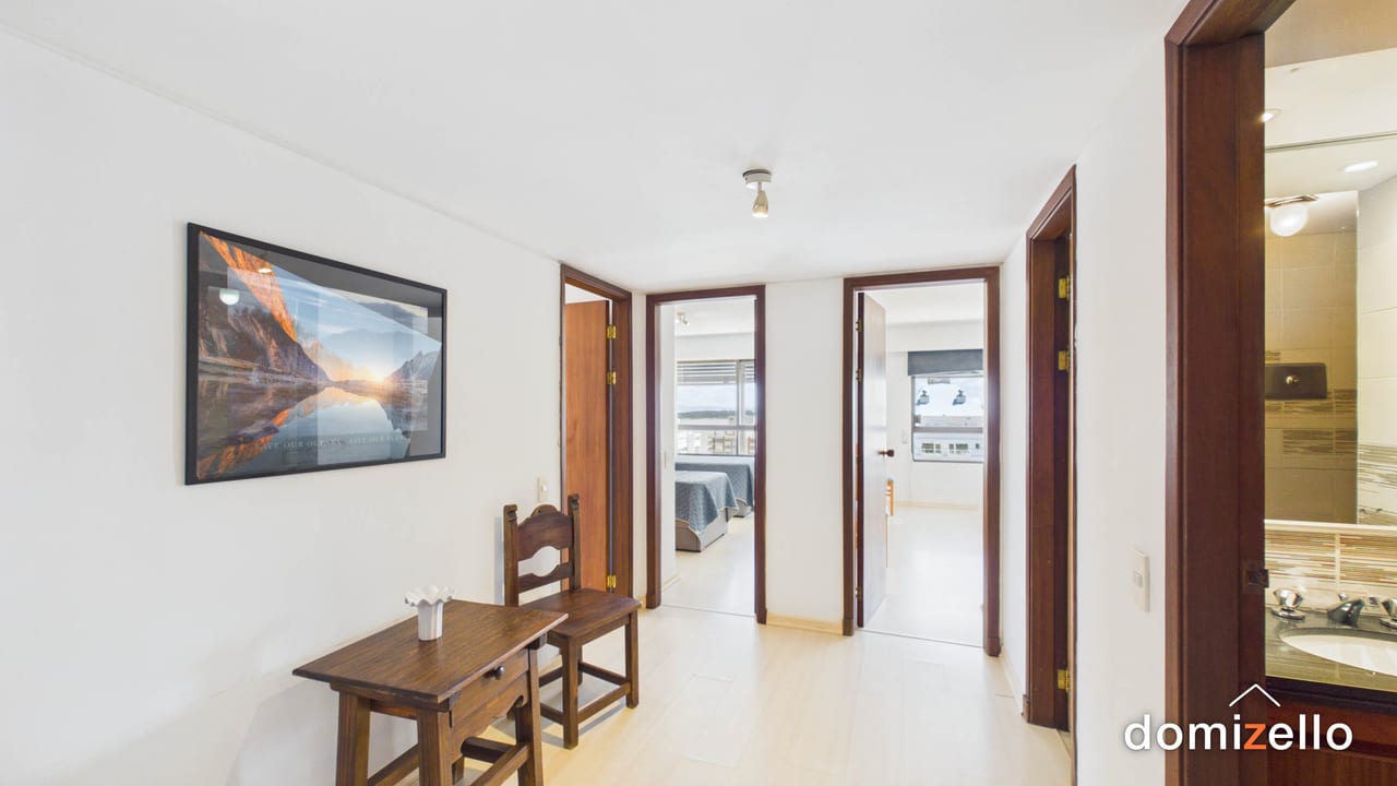 Pasillo con mesa y silla de madera, puertas a dormitorio y baño, apartamento en Peninsula, Punta del Este