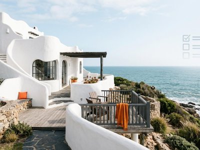 Casa costera estilo Casapueblo en Uruguay con paredes blancas curvas y un sutil gráfico que simboliza listados y amenities.